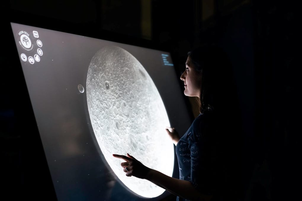 A woman studies a close-up image of the moon displayed on a large computer screen.