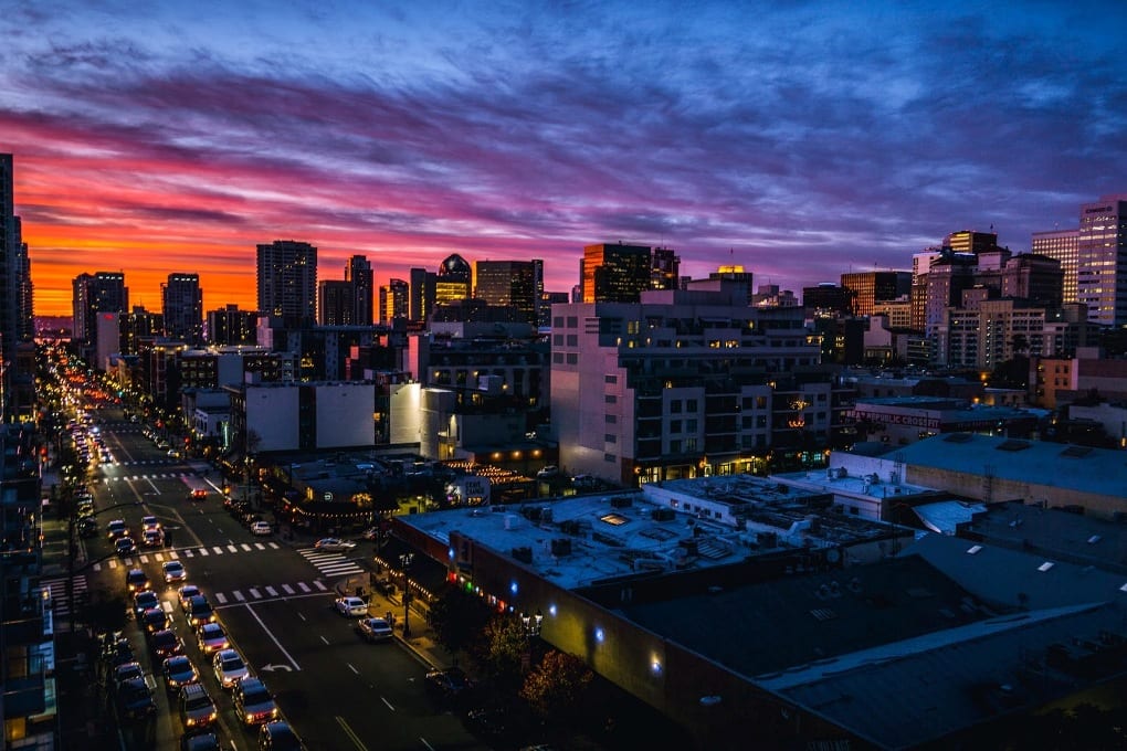 Skyscrapers and other tall buildings loom over a busy street that vanishes into a brilliant orange and pink sunset. 