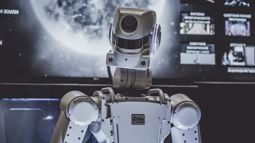 a white robot stands in front of a screen with the moon on it