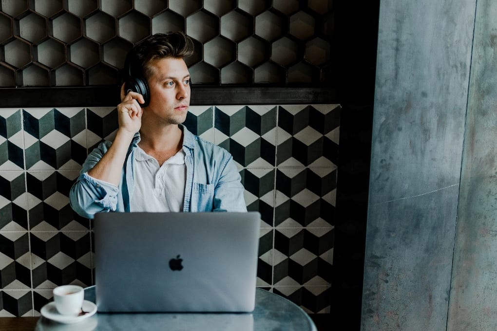 Man sitting against patterned wall wearing headphones and using laptop
