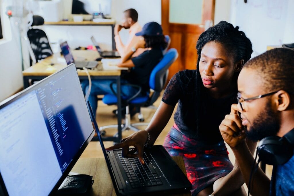 A man and a woman in a library sit in front of a computer screen displaying code. 