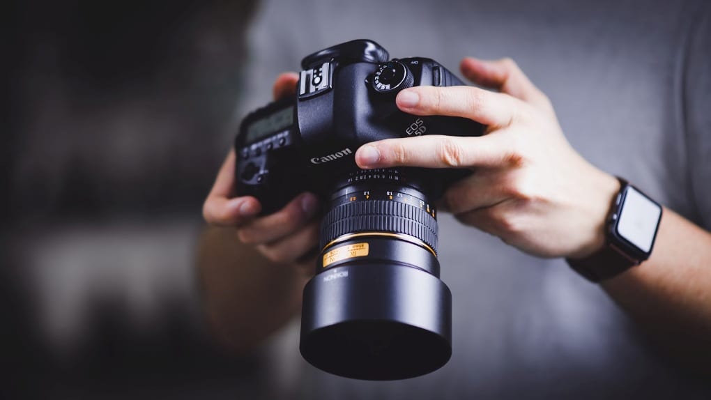 Person wearing smart watch and holding black canon camera