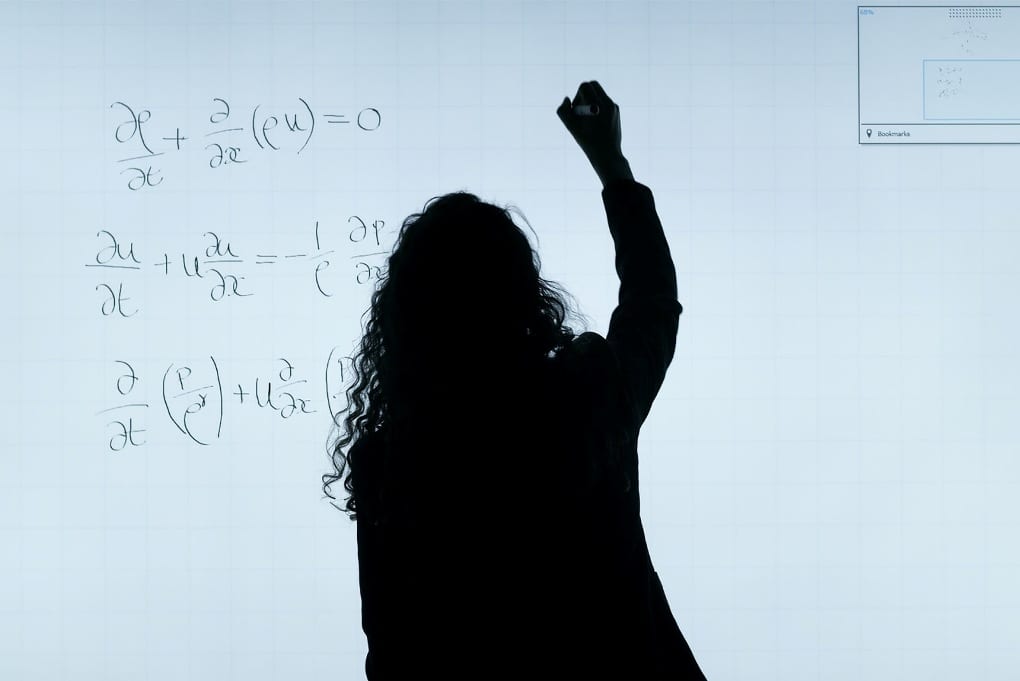 silhouetted person with long curly hair and a raised arm solves math problems on a white board