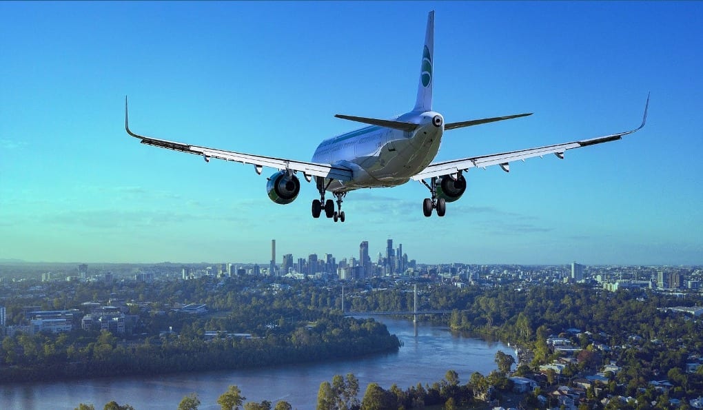 A plane coming in for landing with the silhouette of a city in the background.