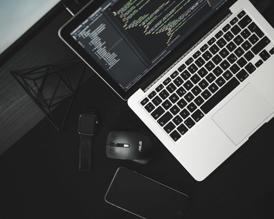 Aerial view of black and silver laptop on black desk next to smartphone and watch