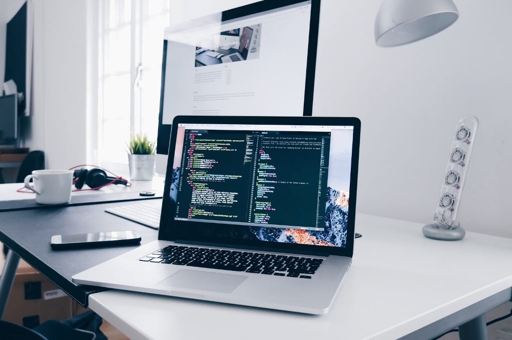 Open silver and black laptop sitting on white desk, displaying code on screen 