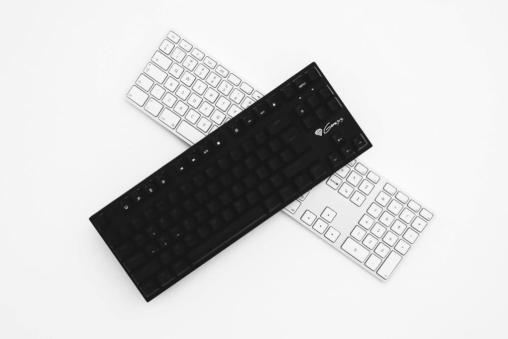 Black keyboard lying diagonally across white keyboard on white background