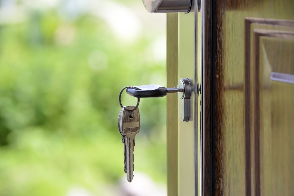 A set of keys hangs from a door that swings open, as the camera faces outside. 