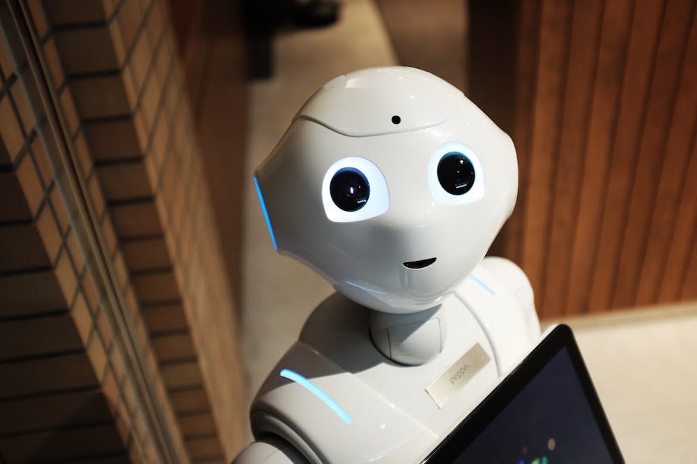 A white humanoid robot smiling at the camera while holding a tablet.