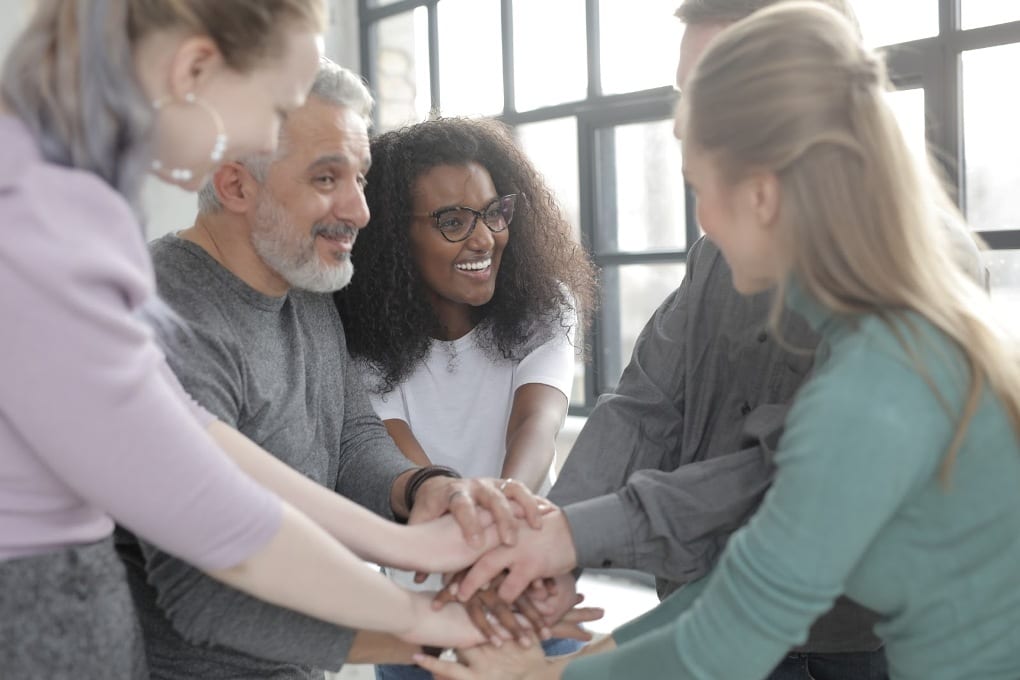 a circle of men and women all putting their hands together in the middle