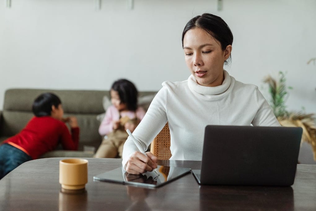 Project manager woman taking notes on her tablet. Her children are behind her.