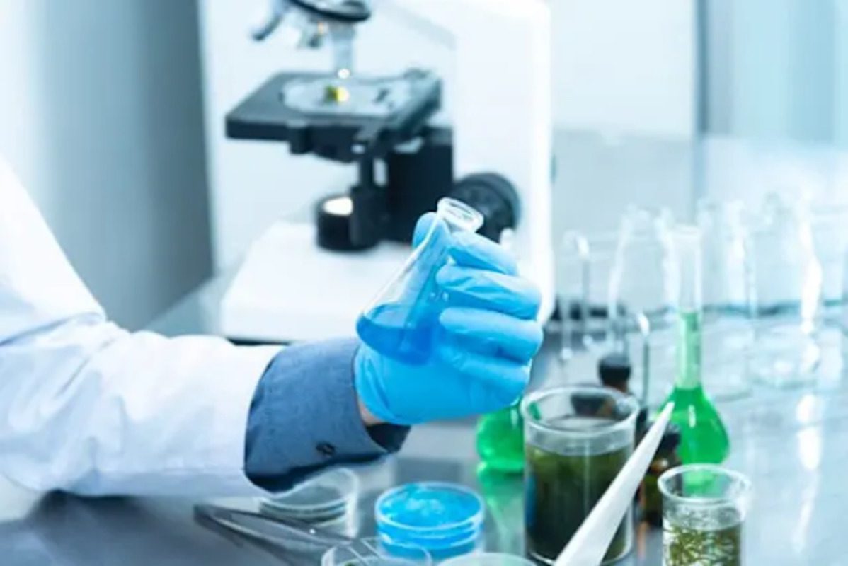 A person in a lab holding a beaker with blue liquid in it. 