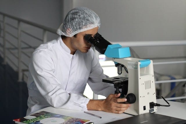  A man in medical gear looking through a microscope. 
