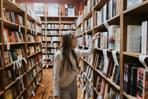 College student wearing glasses and a shite shirt in a library 