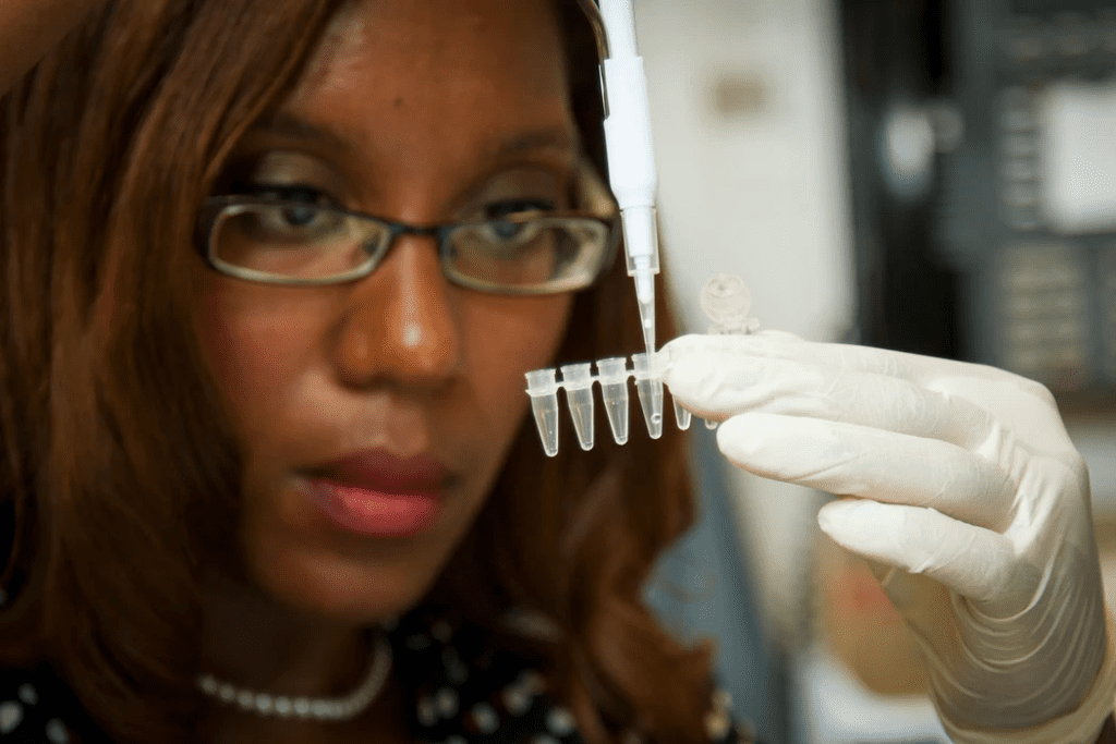 Woman working in a laboratory, holding testing tubes in her hand while wearing a white latex glove. She has spectacles on.