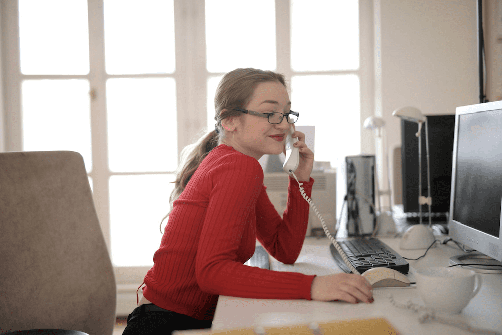 Woman in red sitting at a desk talking on the phone