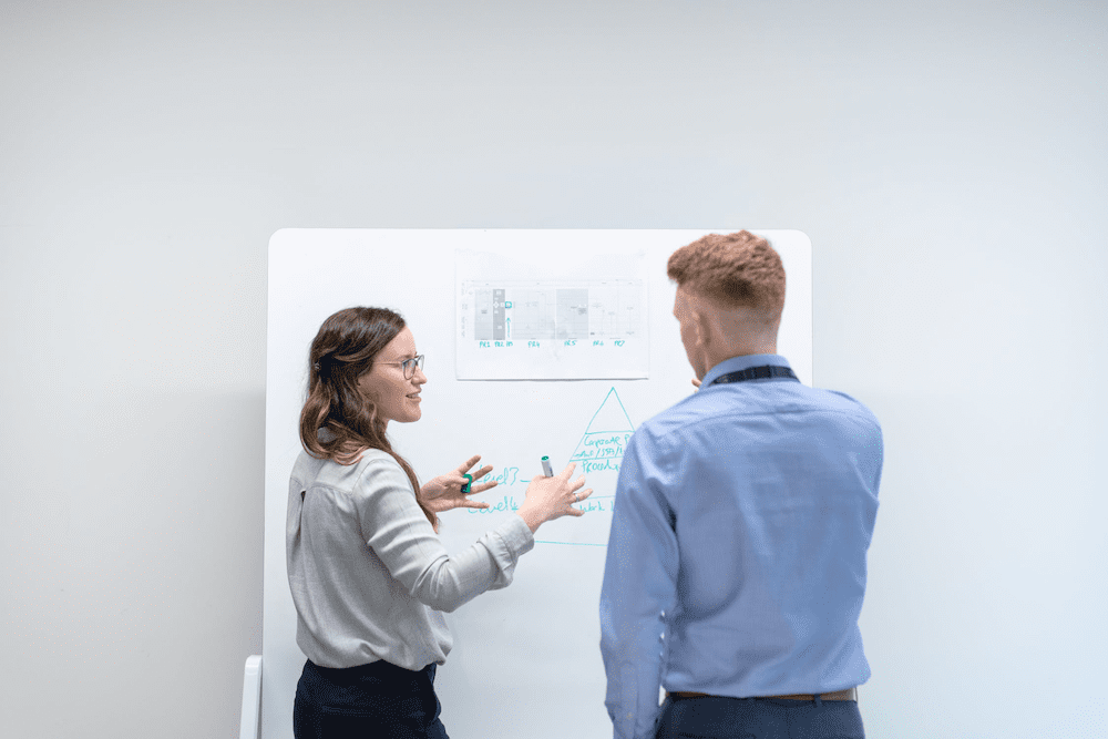 woman showing coworker her work on a whiteboard