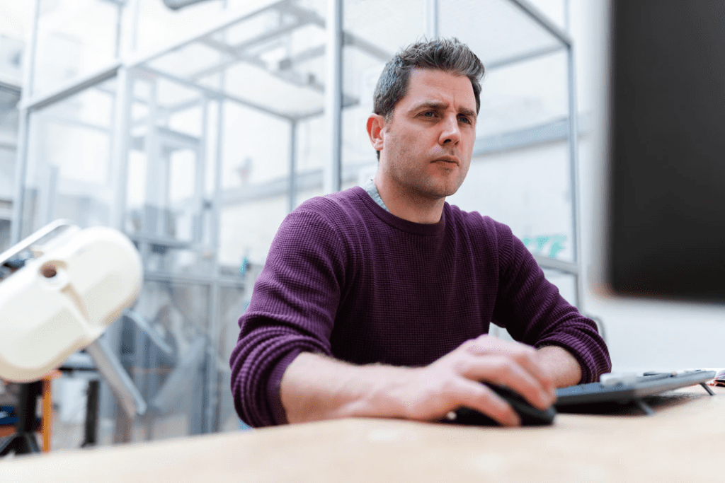 a man in a purple jersey working on his computer. Close up of his hand on his mouse and keyboard next to him.