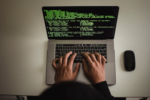 a man types on a silver laptop showing code on the screen