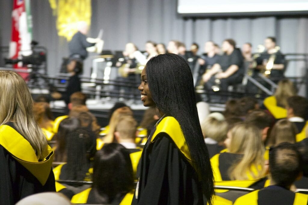 Woman with long black hair wearing black and yellow graduation robes at a graduation ceremony