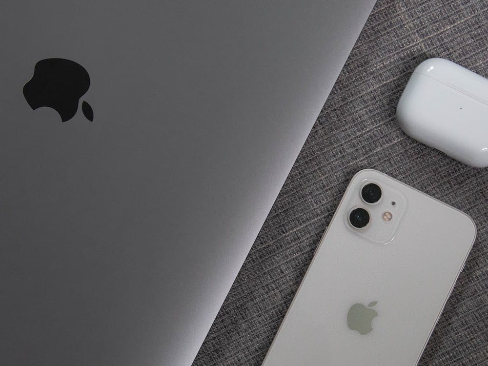 Silver Macbook next to white iPhone and Airpods on grey background