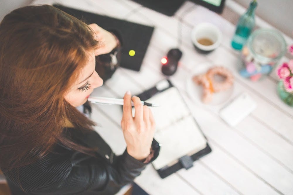 a young lady thinking while taking notes