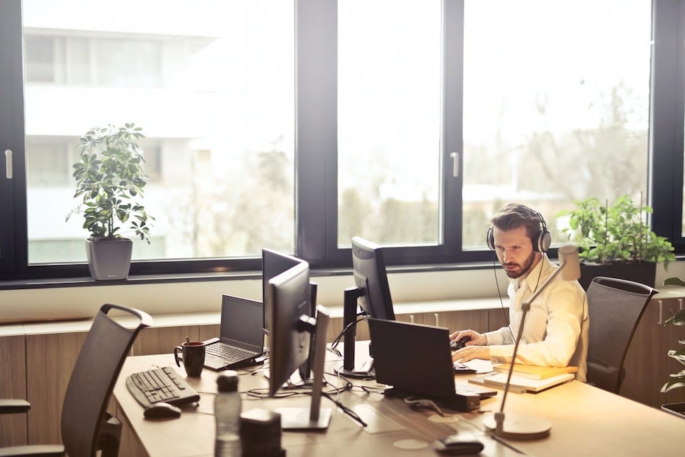 A man works at his computer in an office by a sunny window