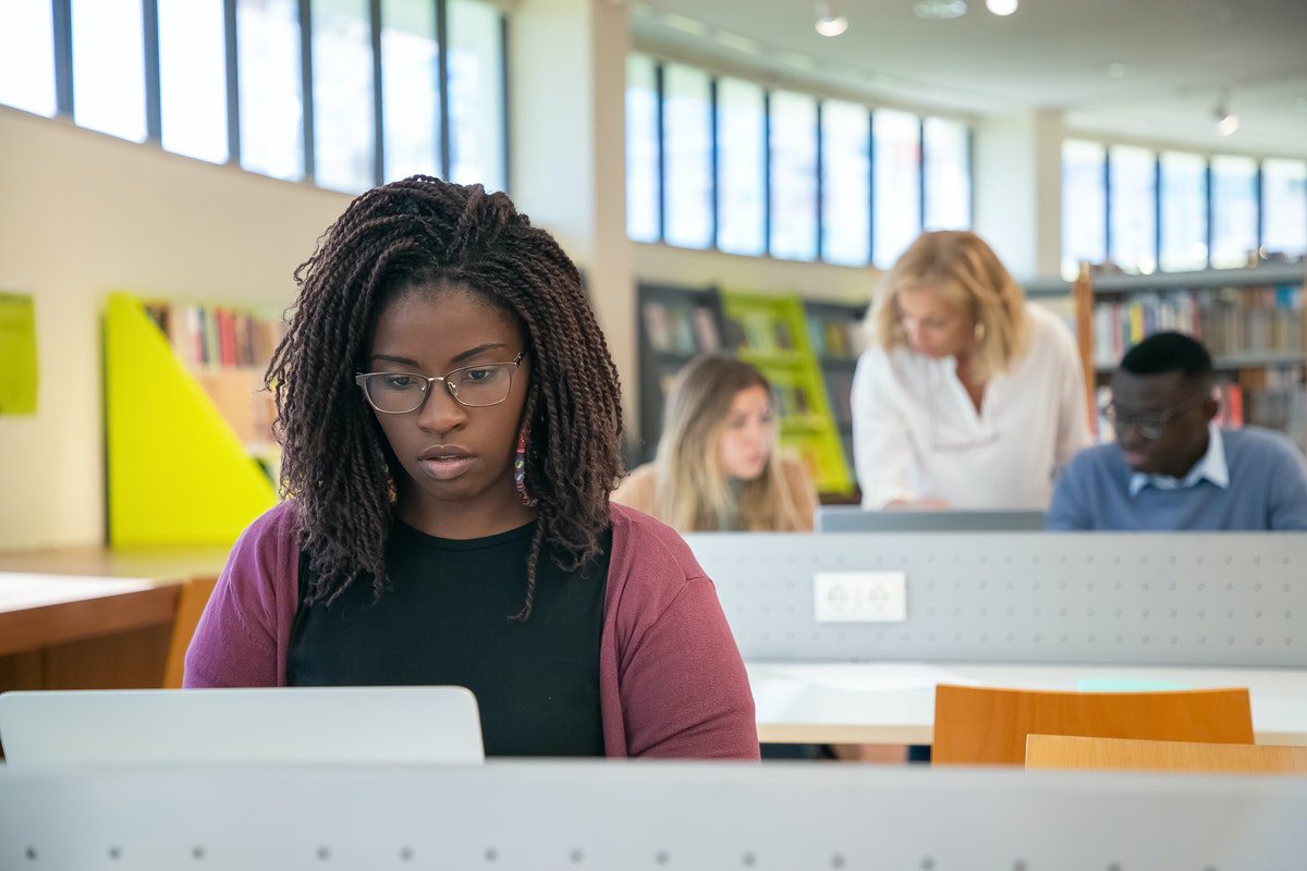 young female college student working in the library on homework for her postsecondary classes How to Become an IT Support Specialist