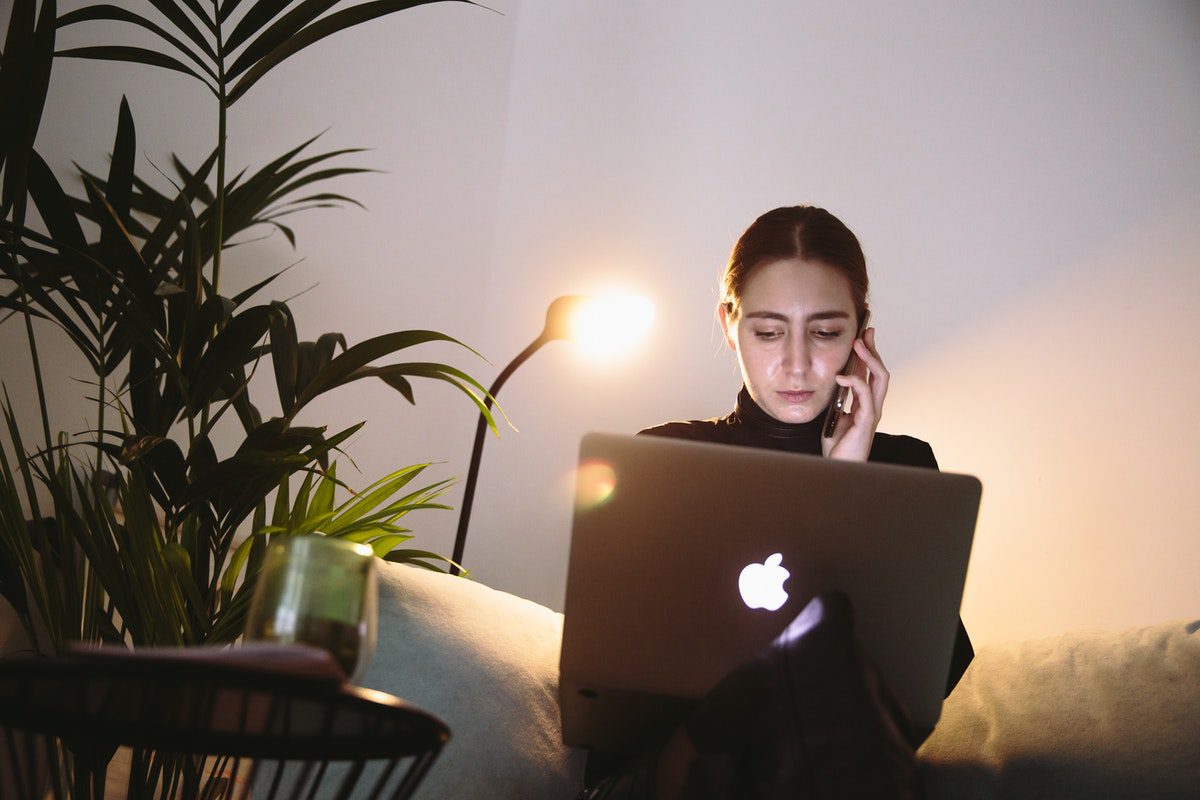 Woman talking on the phone while sitting with a laptop on her lap How to Become an Information Systems Analyst