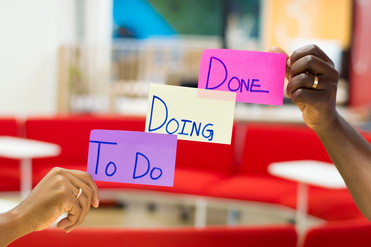 Two hands hold up pieces of paper with “to do,” “doing,” and “done” written on them. How to Become a Scrum Master