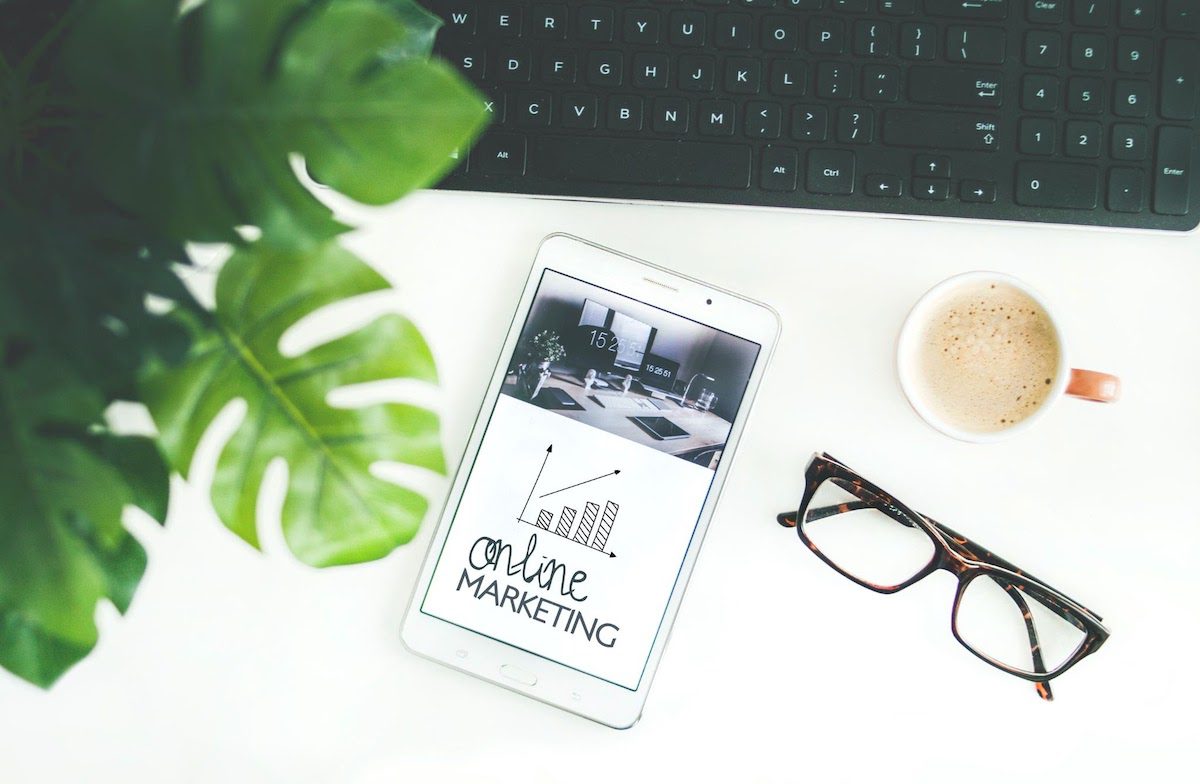 A smartphone, framed eyeglasses, and coffee cup next to a computer keyboard how to become a content marketer