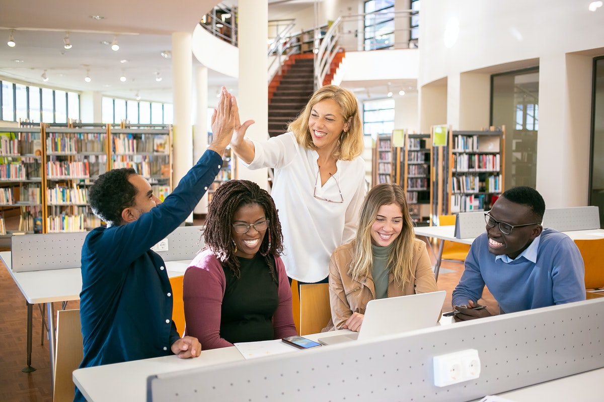  Group of happy students in a library with one person giving the teacher a high five how to become a financial analyst