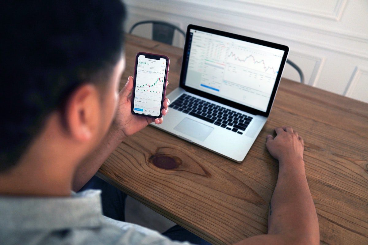 A man studying a progression graph on his iPhone and Macbook How to Become a Quantitative Analyst