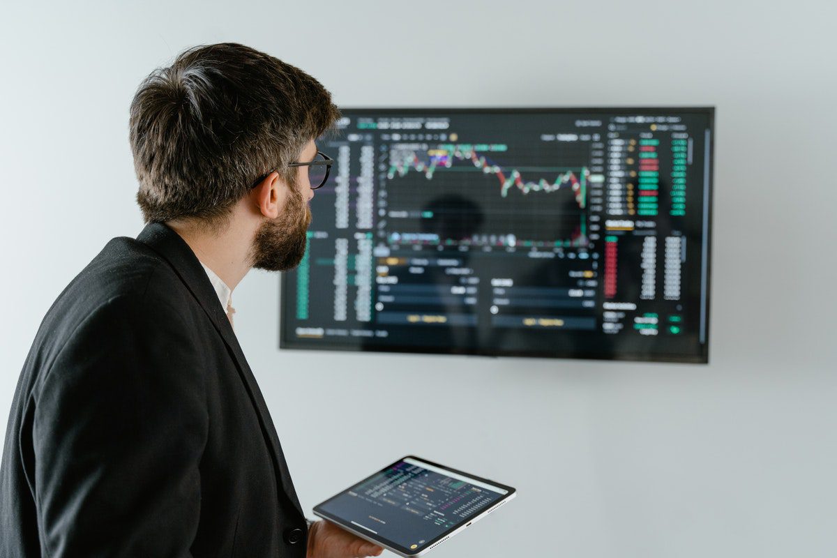 A man holding a digital tablet and staring at data on a larger screen. Data Analytics Master's Degrees