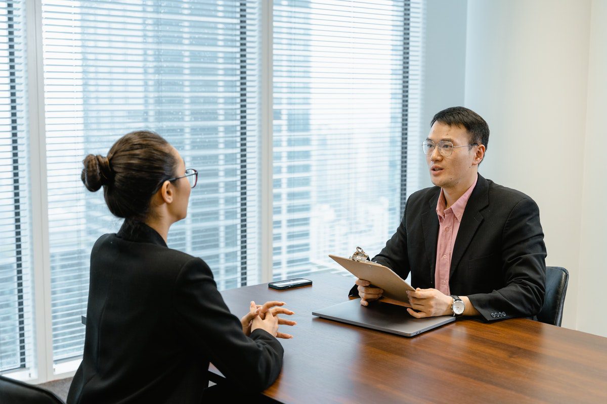  a man in a black suit holding a folder while talking to an interviewee Common Computer Technician Interview Questions and How to Answer Them 