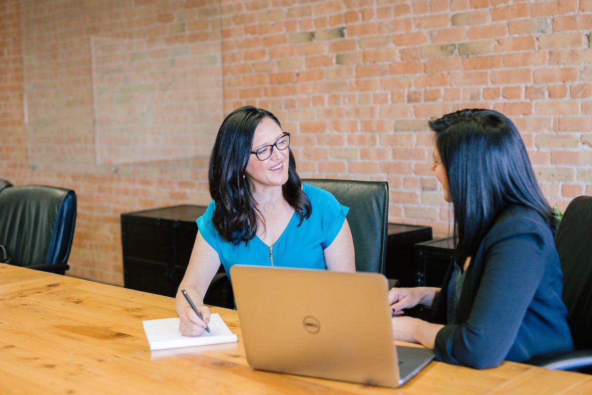 Two smiling women with a laptop on the table. Sales Coordinator Interview Questions and Answers