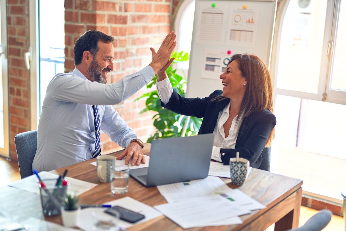 A man and woman smiling and giving a high five in an office. Administrative Assistant Interview Questions and Answers