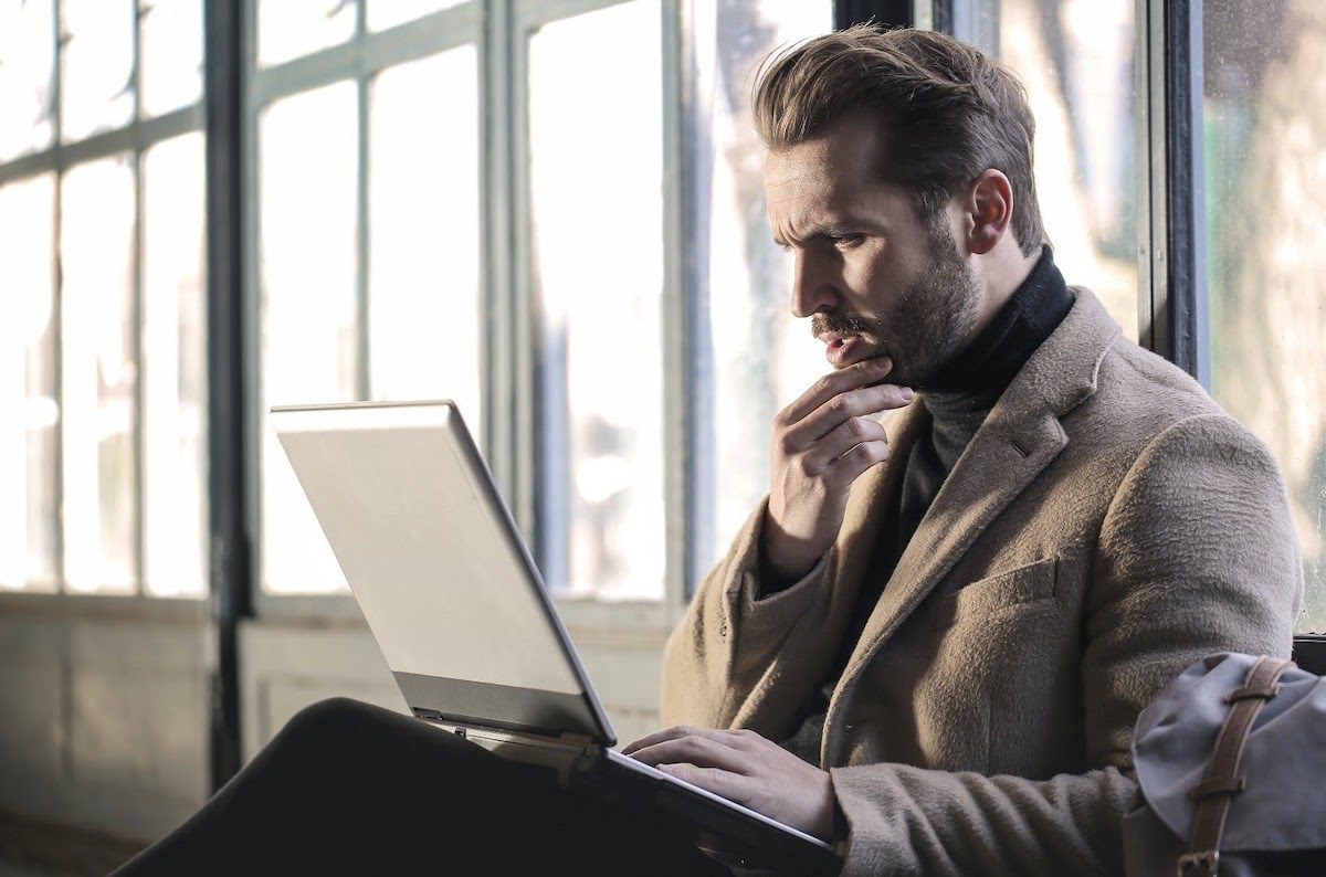 Coder in suit looking inquisitively at a laptop.