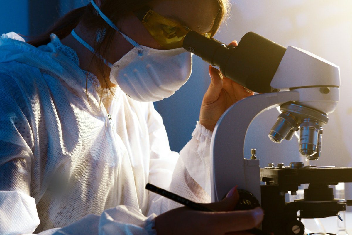  A biochemist wearing a mask using a microscope. Jobs for Biochemistry Majors