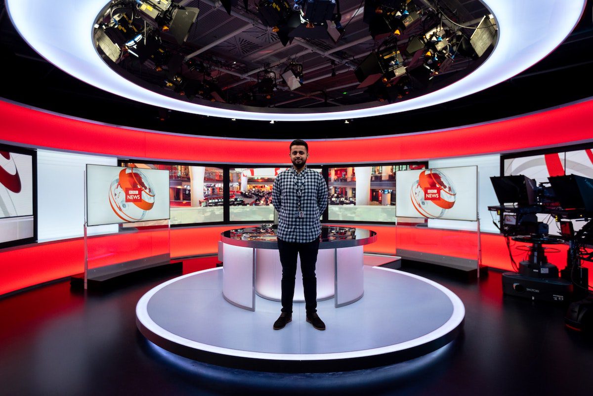 A person in a black and white check shirt standing at the BBC news broadcasting section. Jobs for Communications Majors