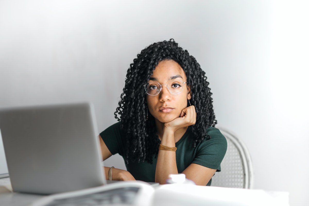 A woman with a serious expression sits at a table with her laptop.