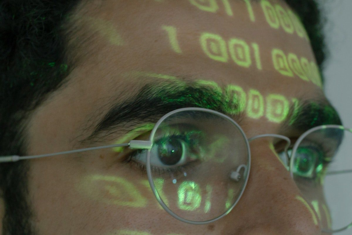 A close-up of a person wearing glasses with binary code projected on their forehead.