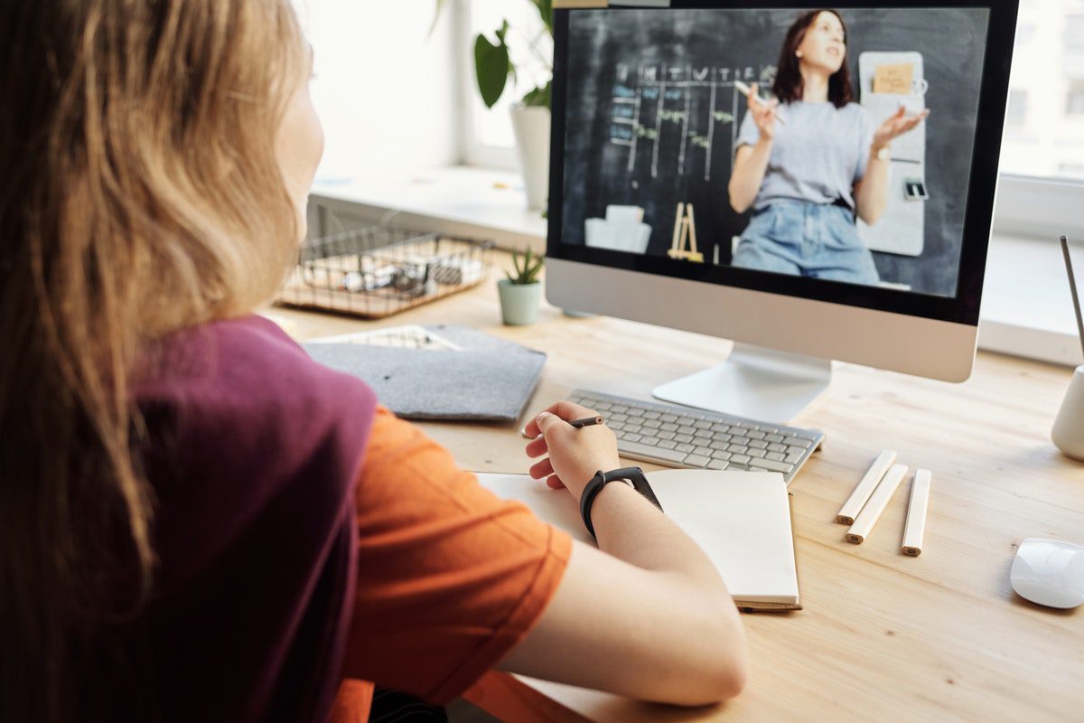 a girl in an orange shirt watching a lecture on a monitor in her spare time. Online Tech Courses