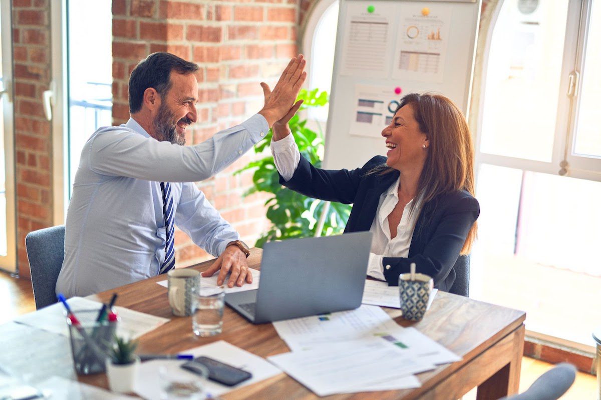 Two happy business workers giving each other a high five at the office.