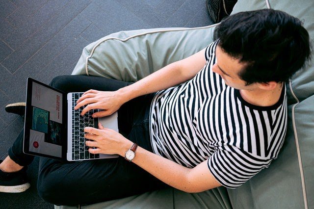 Man sitting on a beanbag chair while on his laptop 