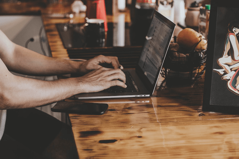 Hands typing on a laptop sitting on a crowded table. 