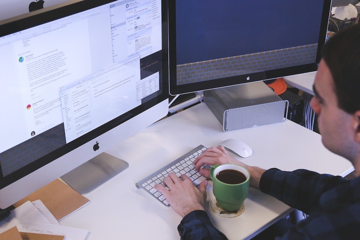 a man sitting in front of two desktop monitors looking at a project overview