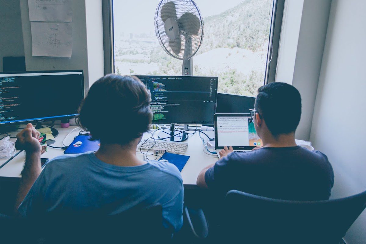 Two individuals working in front of several computer screens.