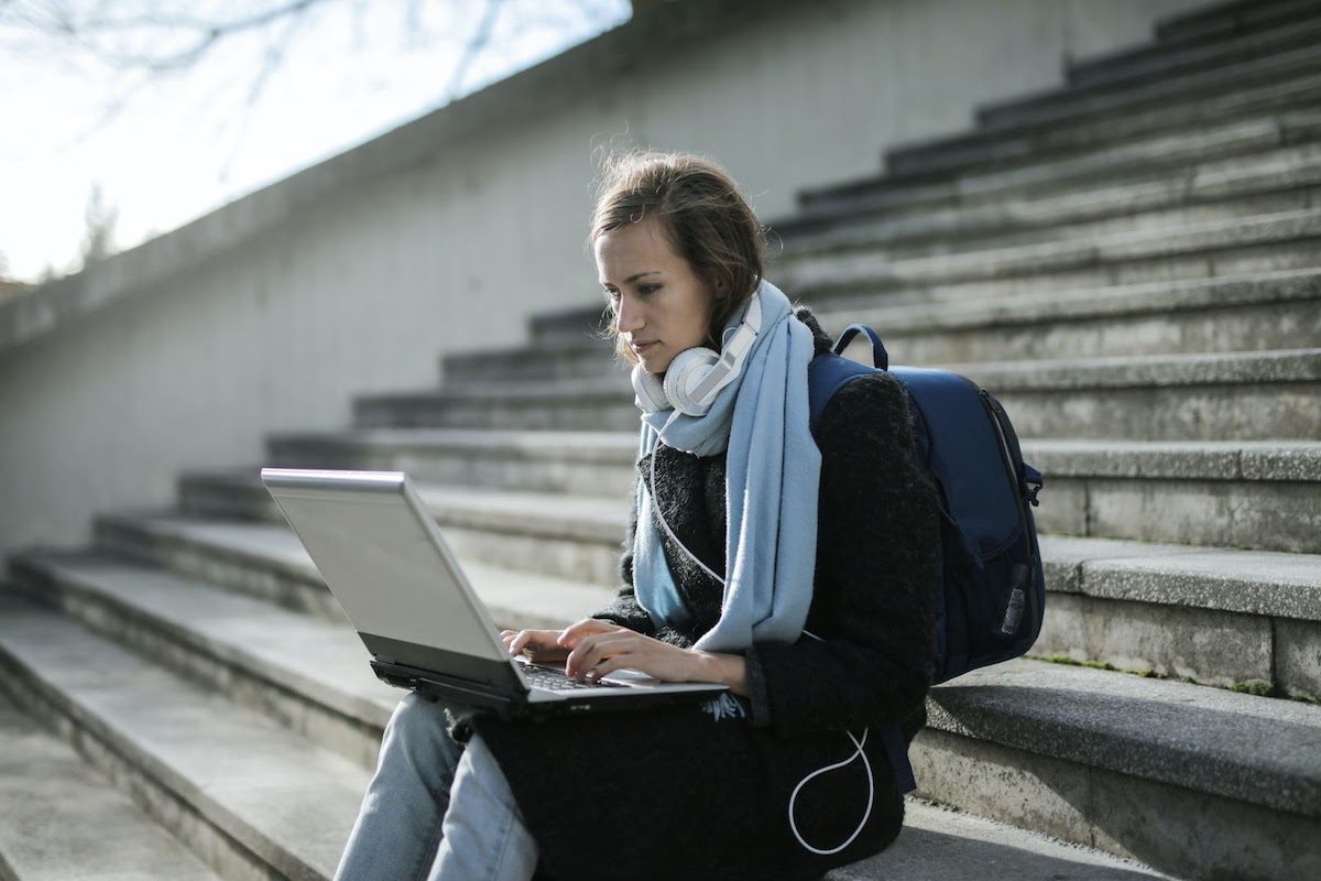 A person wearing headphones and a backpack using a laptop on cement stairs Database Management Bachelor's Degrees