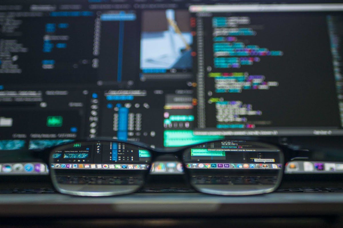 A pair of eyeglasses is posed in front of two laptops displaying code